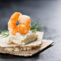 Appetizer canape with shrimp, cheese and dill on a small loaf of bread, closeup with copy space